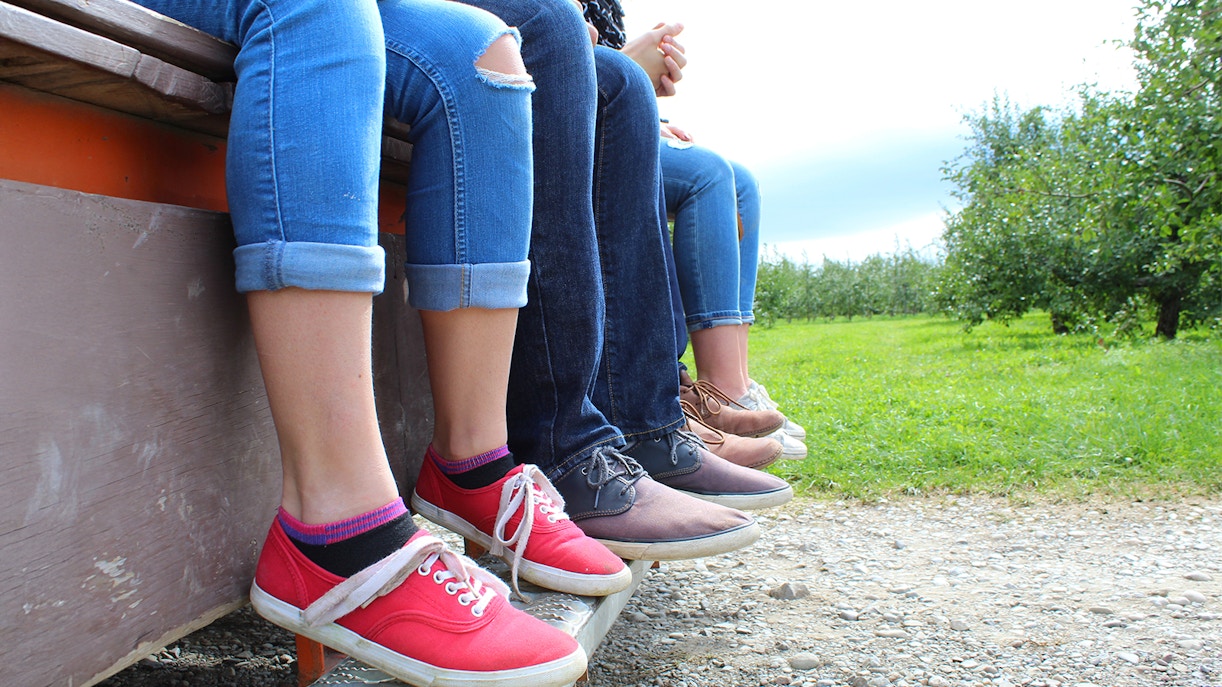 Casual shoes worn by people sitting on a bench in an orchard.