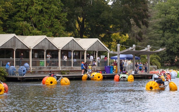 Visitors enjoying pedal boats on a lake near a pavilion during the Puffing Billy and Phillip Island tour.