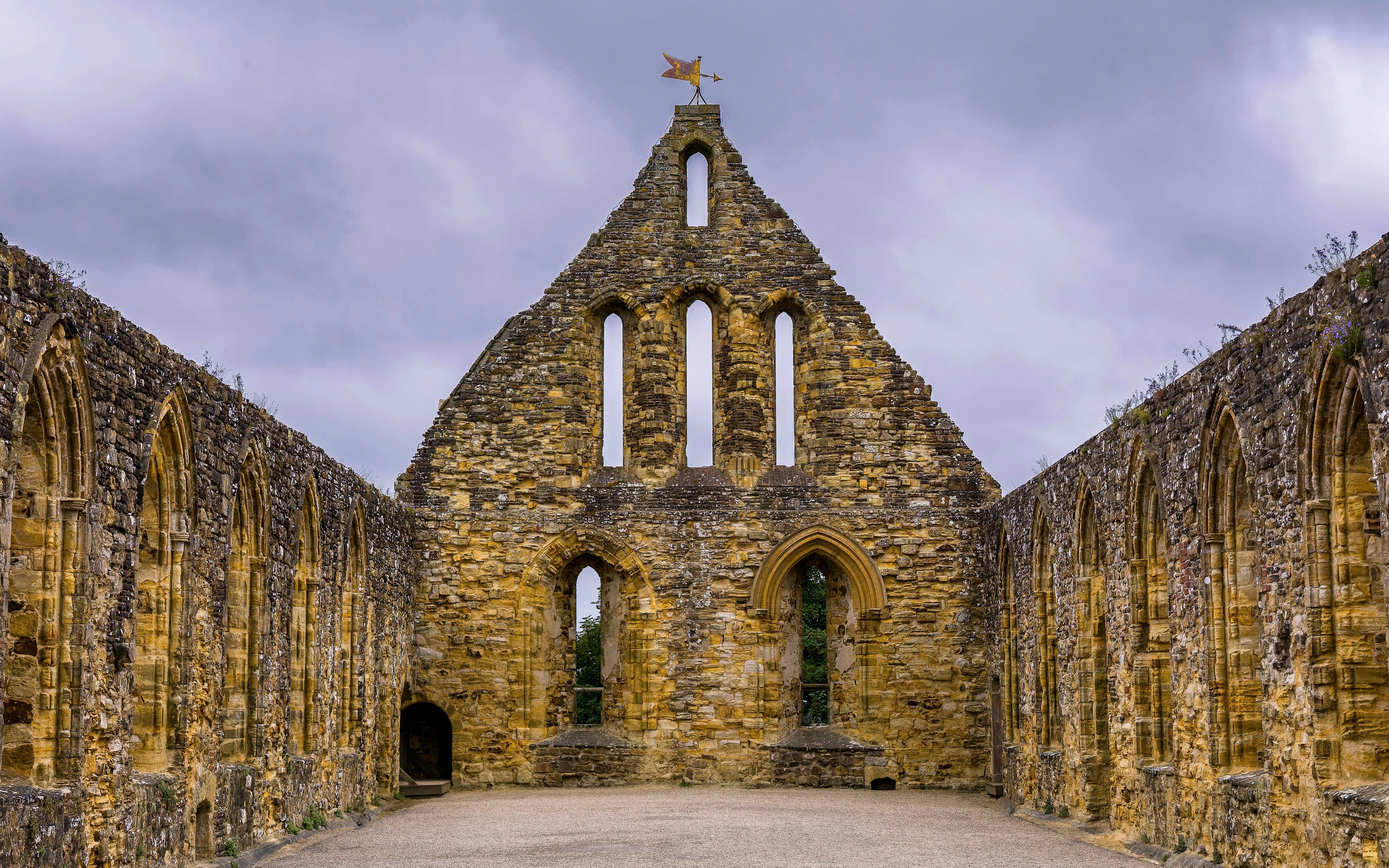 Historic stone ruins of Battle Abbey dormitory under cloudy sky in Battle, England.
