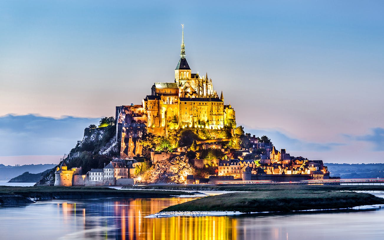 Mont-Saint-Michel Abbey illuminated at night, reflecting in the water.