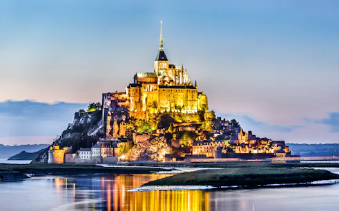 Mont-Saint-Michel Abbey illuminated at night, reflecting in the water.