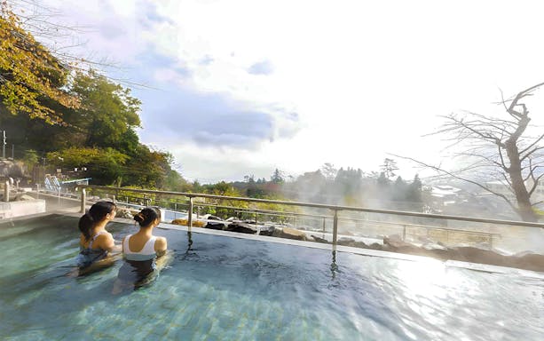 Two people enjoying an outdoor hot spring at Hakone Kowakien Yunessun, Japan.