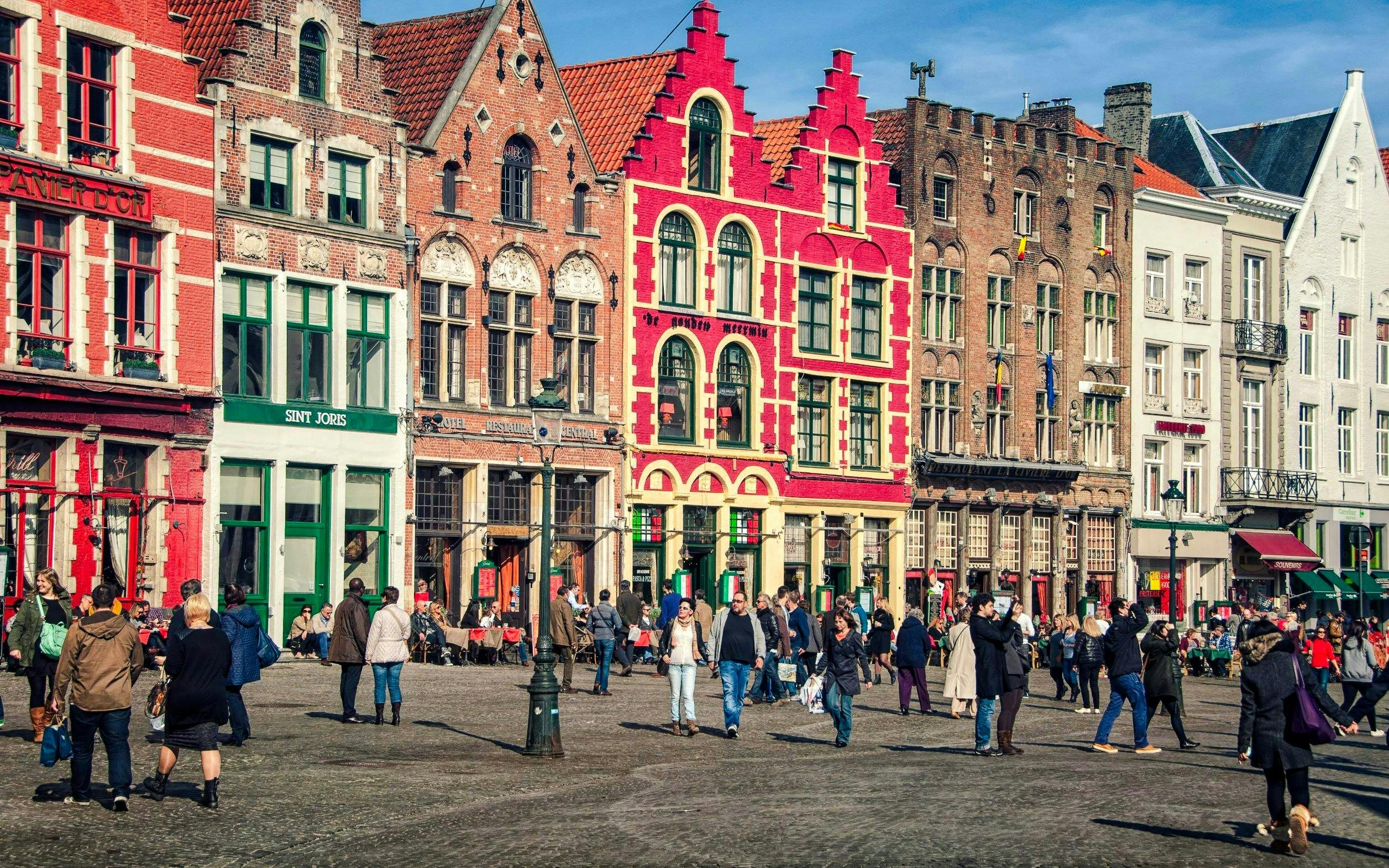 Crowd at Grote Markt in Bruges, Belgium, with historic gabled buildings in the background.
