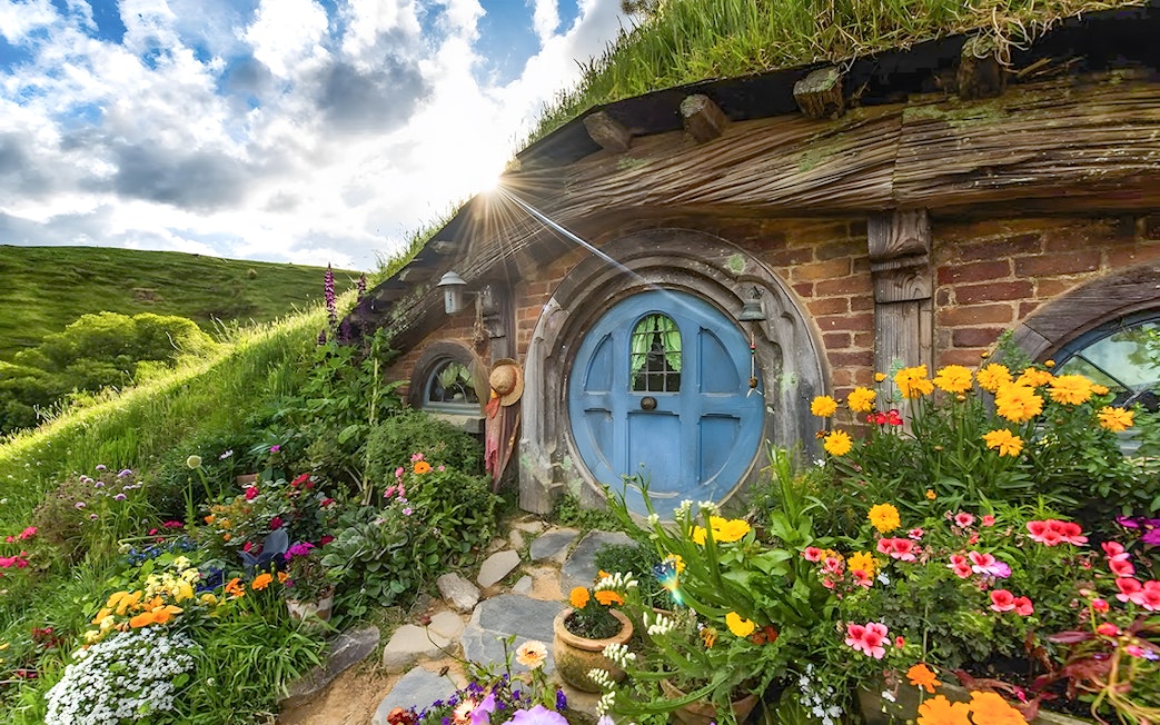 Hobbiton house with blue door and vibrant flowers, lush greenery in Rotorua.