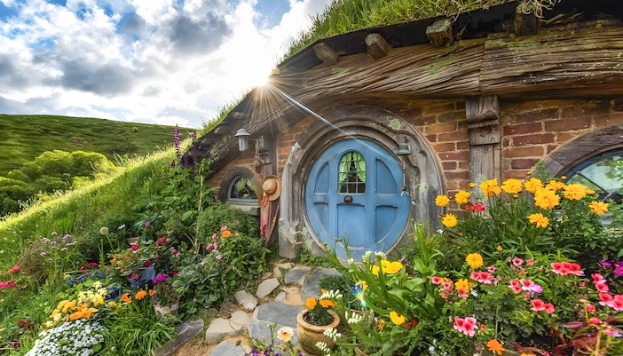 Hobbiton house with blue door and vibrant flowers, lush greenery in Rotorua.