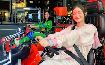 Two people in costumes driving go-karts on a street in Osaka Namba at night.