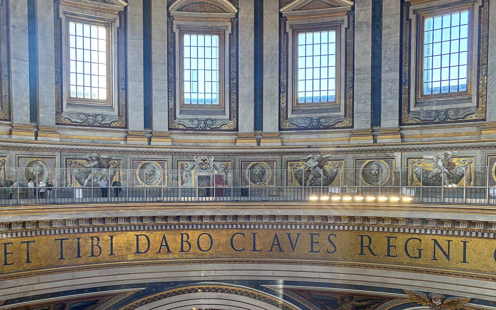 Interior view of St. Peter's Basilica dome with Latin inscription and visitors on the balcony.