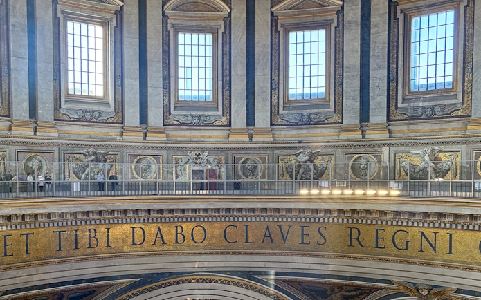Interior view of St. Peter's Basilica dome with Latin inscription and visitors on the balcony.