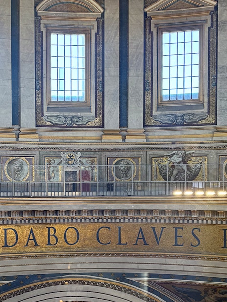 Interior view of St. Peter's Basilica dome with Latin inscription and visitors on the balcony.