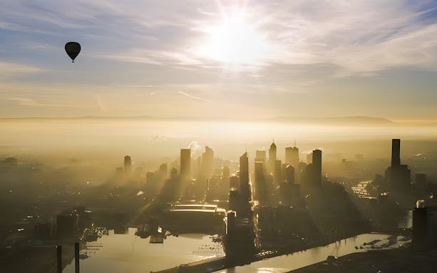 Hot air balloon floating over Melbourne skyline at sunrise.