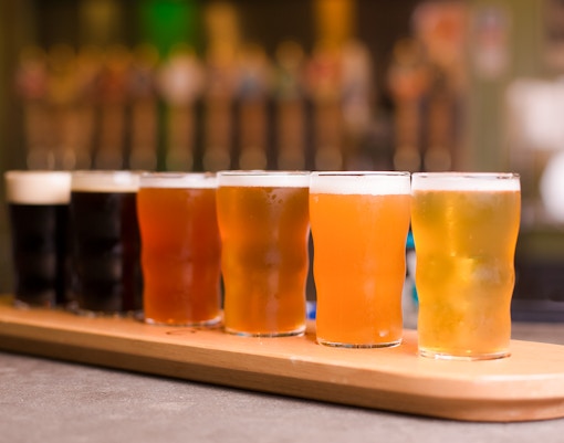 Rainbow color beer taster tray with six different beers on a wooden board.