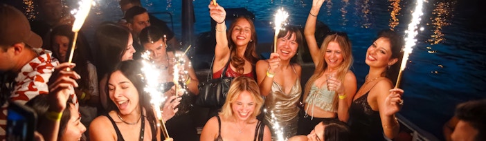 Group celebrating with sparklers on a boat cruise at dusk.