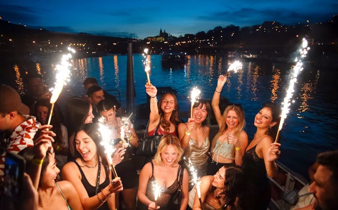 Group celebrating with sparklers on a boat cruise at dusk.