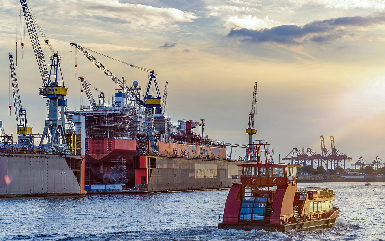Harbor boat passing shipyard cranes during sunset on 1h tour with live commentary.