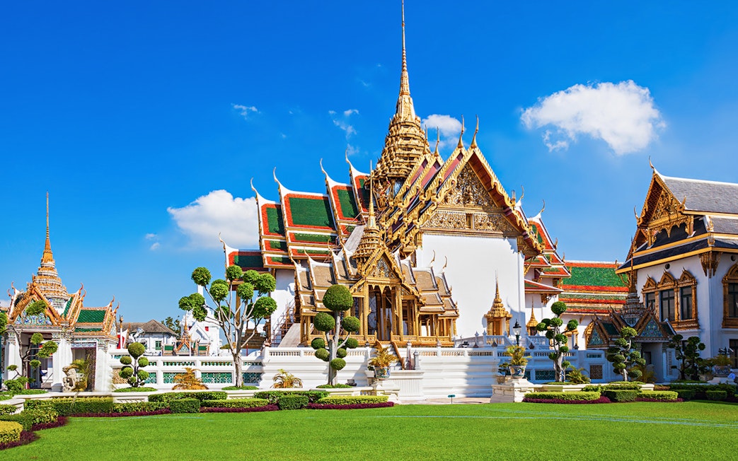 Grand Palace in Bangkok with ornate architecture and manicured gardens.