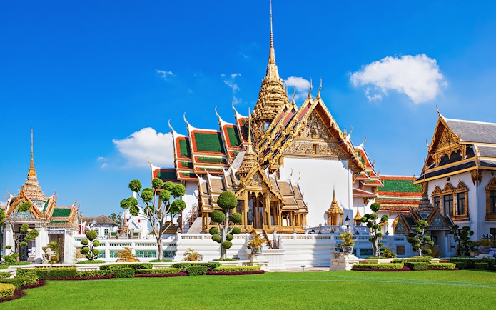 Grand Palace in Bangkok with ornate architecture and manicured gardens.