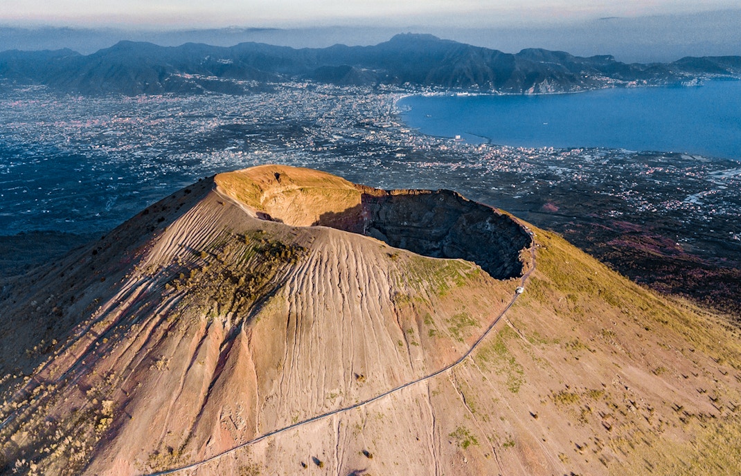 Aerial view of Mount Vesuvius crater with Naples and coastline in the background.