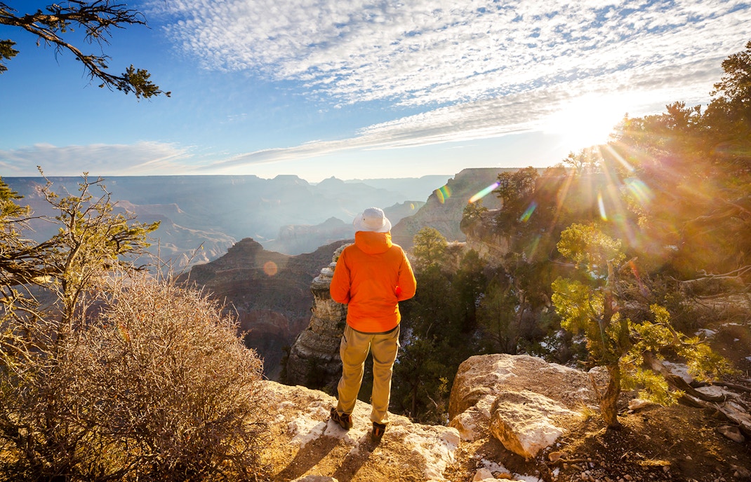 Person standing on Grand Canyon edge at sunrise, overlooking vast canyon landscape.