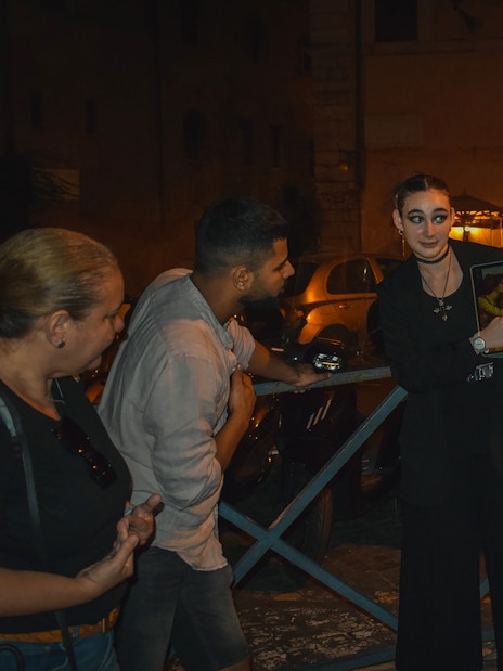 Tour guide showing a tablet to a group during a ghost walking tour in Rome at night.