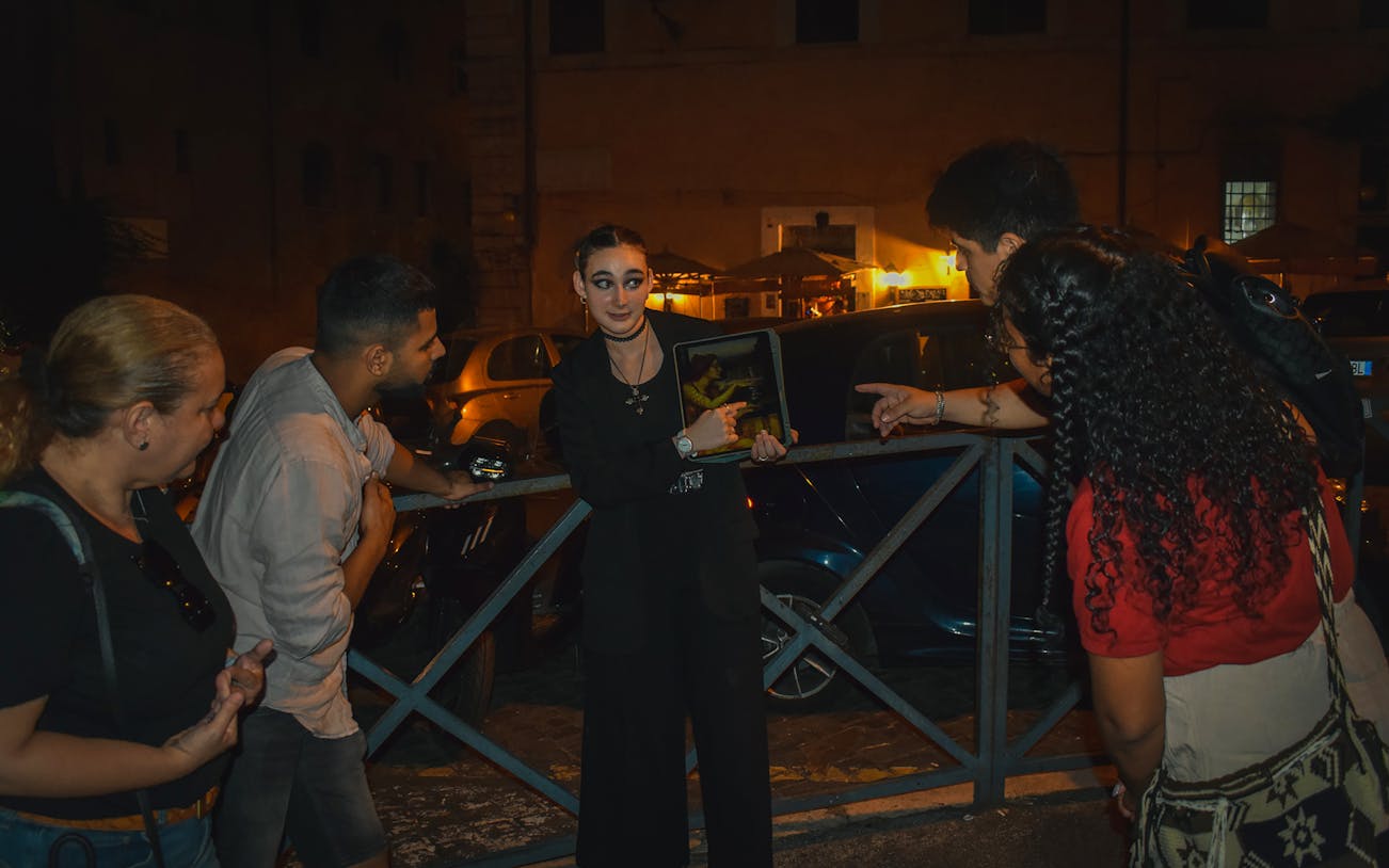Tour guide showing a tablet to a group during a ghost walking tour in Rome at night.