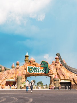Entrance to Dino Desert theme park with dinosaur sculptures and visitors walking.