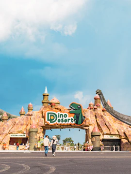 Entrance to Dino Desert theme park with dinosaur sculptures and visitors walking.