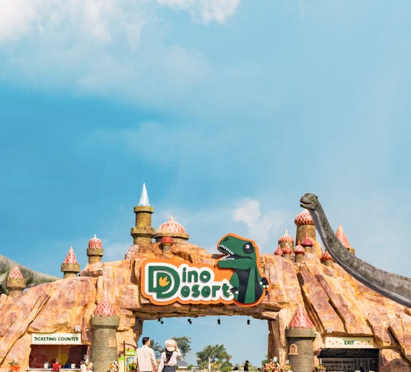 Entrance to Dino Desert theme park with dinosaur sculptures and visitors walking.