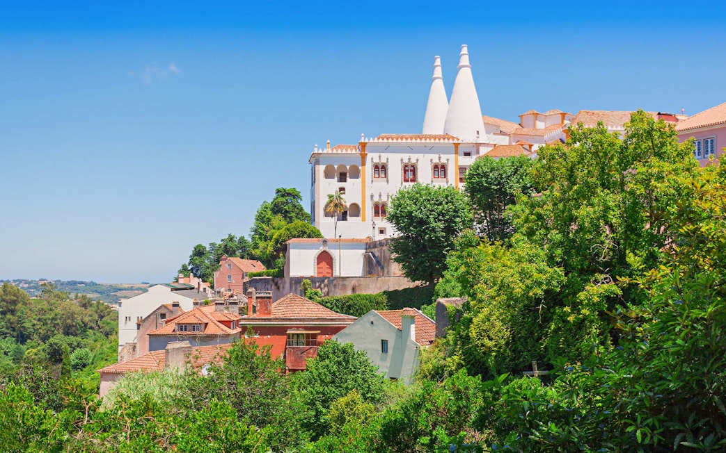 National Sintra Palace with iconic chimneys surrounded by lush greenery in Sintra, Portugal.