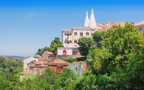 National Sintra Palace with iconic chimneys surrounded by lush greenery in Sintra, Portugal.