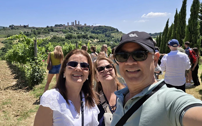 Tourists enjoying a vineyard in Tuscany with San Gimignano towers in the background.
