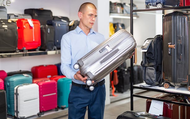 Man placing suitcase on store shelf with various luggage options.