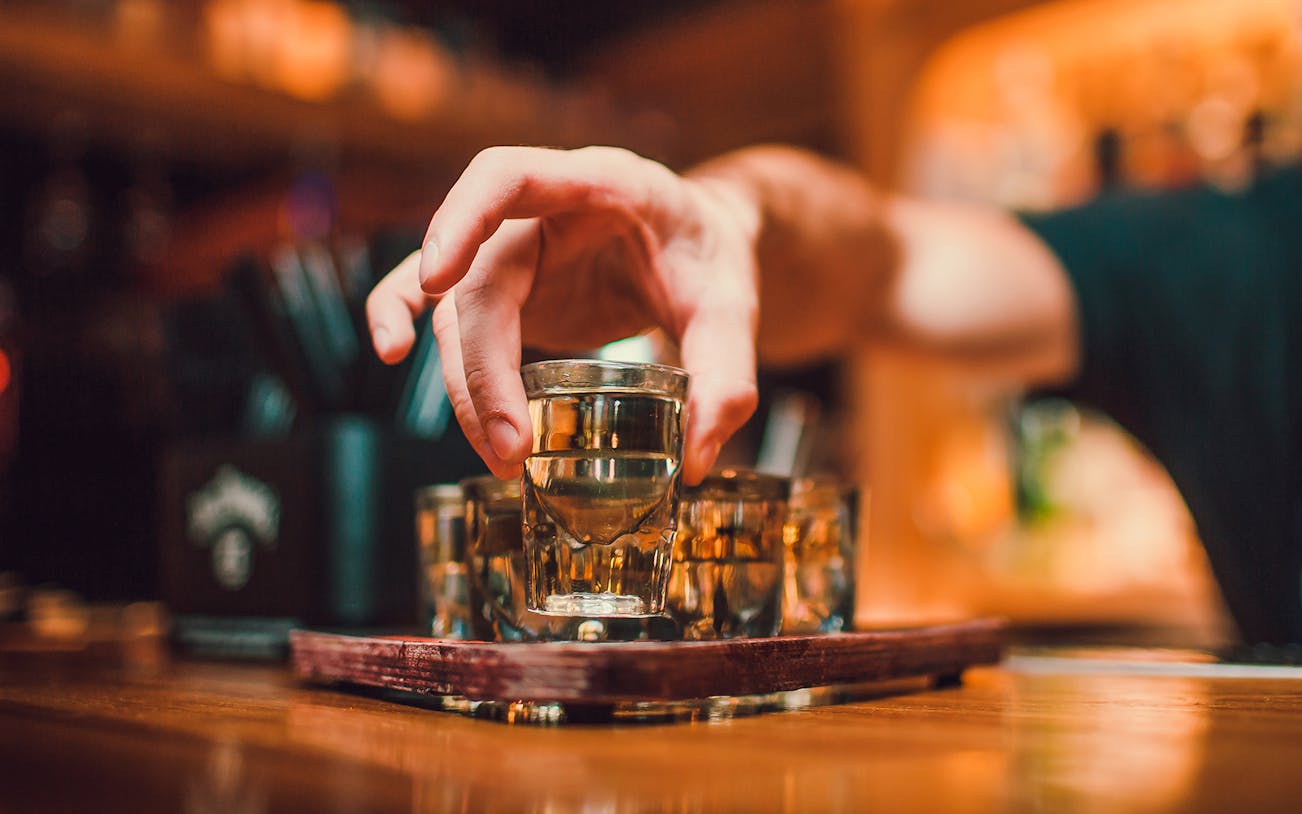 Hand reaching for a vodka shot glass during a tasting session in Wroclaw.