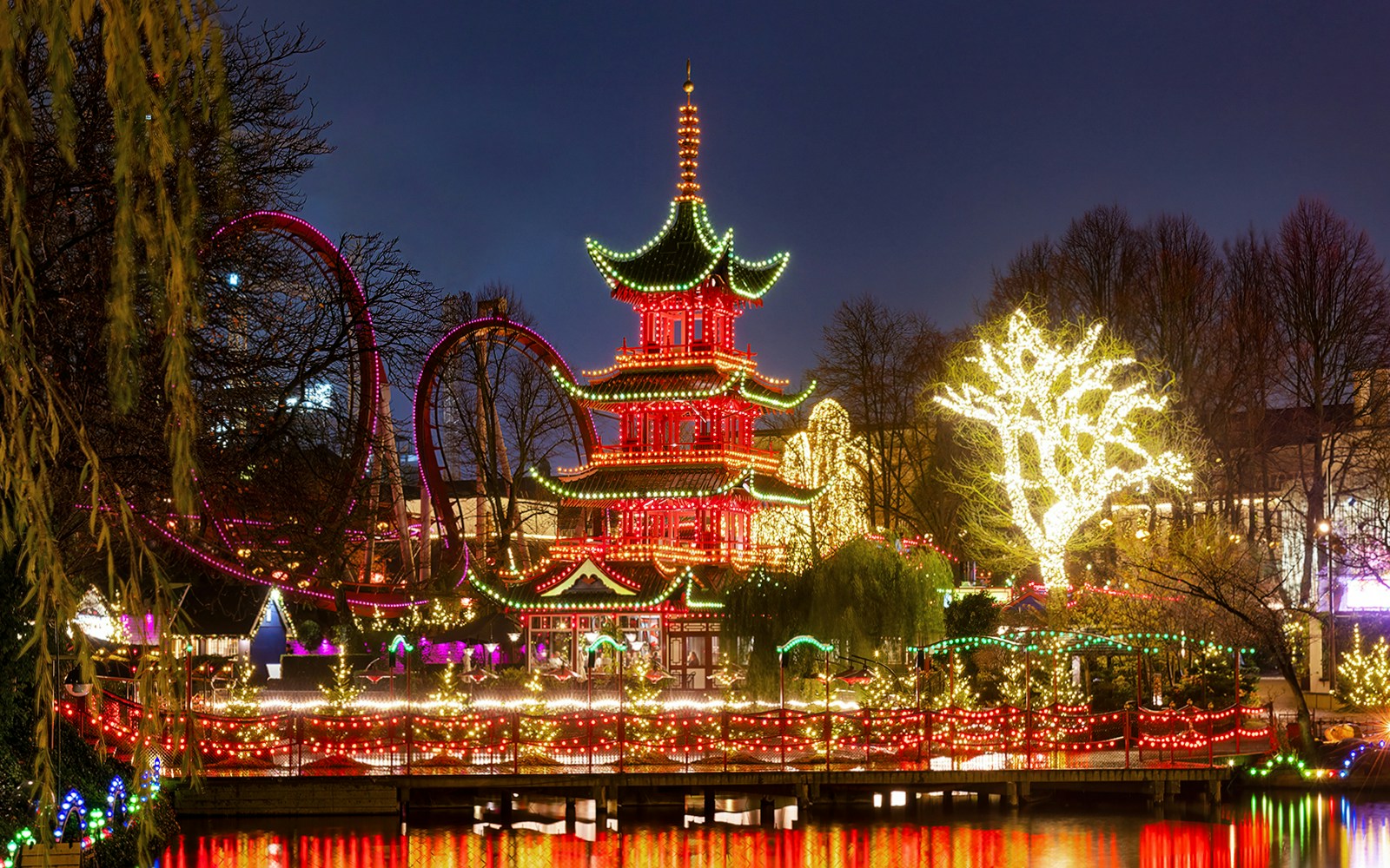 Tivoli Gardens illuminated at night, featuring a pagoda and roller coaster in Copenhagen.