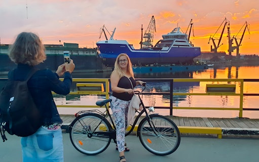 Person on a bike at Gdansk shipyard during sunset, with cranes and a ship in the background.