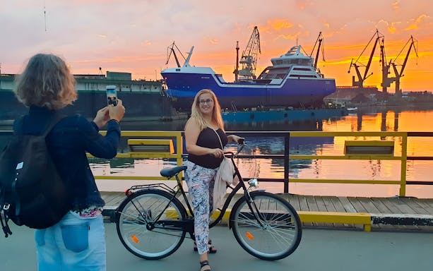 Person on a bike at Gdansk shipyard during sunset, with cranes and a ship in the background.