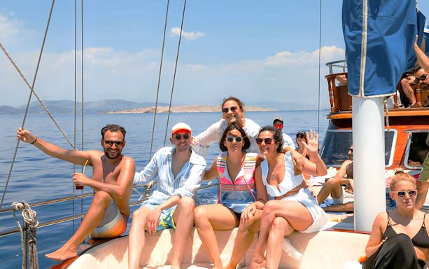 Group enjoying a boat cruise in Athens with clear blue water and distant islands.