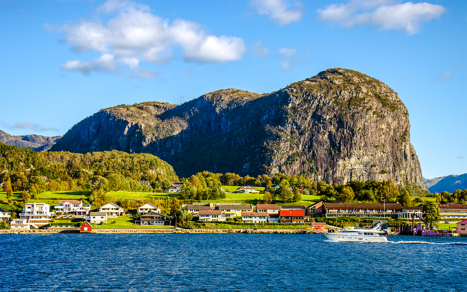Houses along the shore with a boat on Lysefjord, Norway, and rocky cliffs in the background.