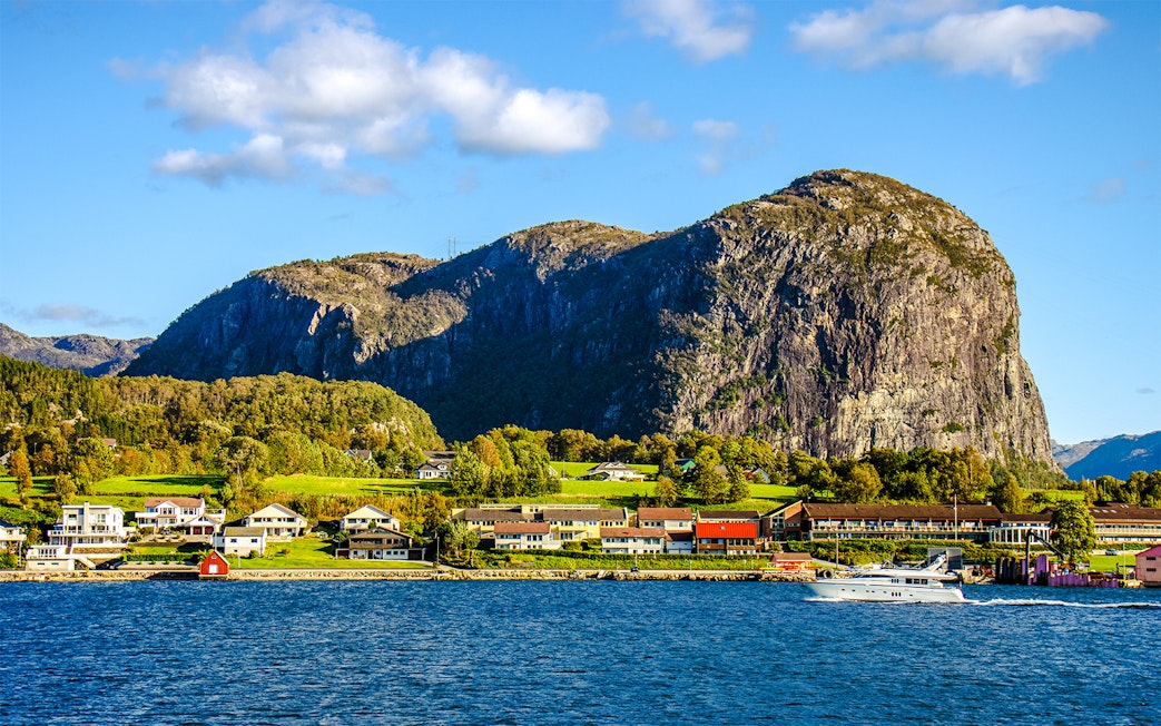 Houses along the shore with a boat on Lysefjord, Norway, and rocky cliffs in the background.