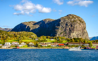 Houses along the shore with a boat on Lysefjord, Norway, and rocky cliffs in the background.