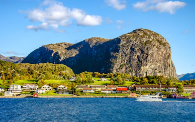 Houses along the shore with a boat on Lysefjord, Norway, and rocky cliffs in the background.
