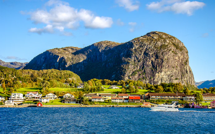 Houses along the shore with a boat on Lysefjord, Norway, and rocky cliffs in the background.