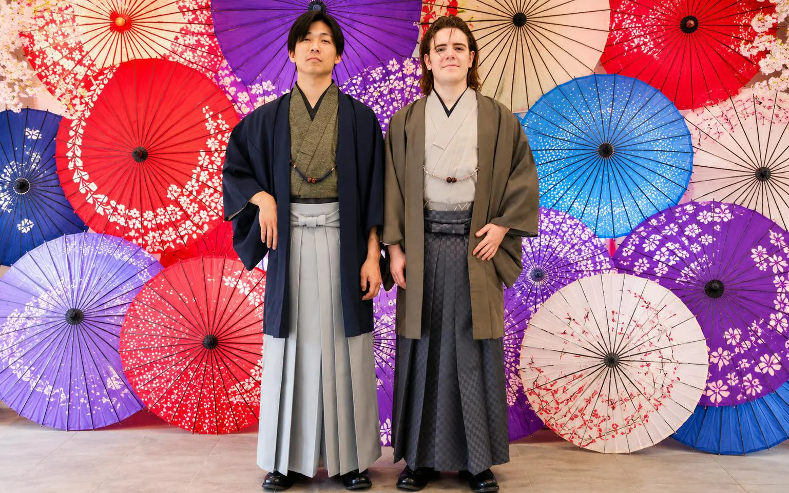 Tourists in traditional kimonos at Rental Kimono Okamoto, standing before colorful parasols.