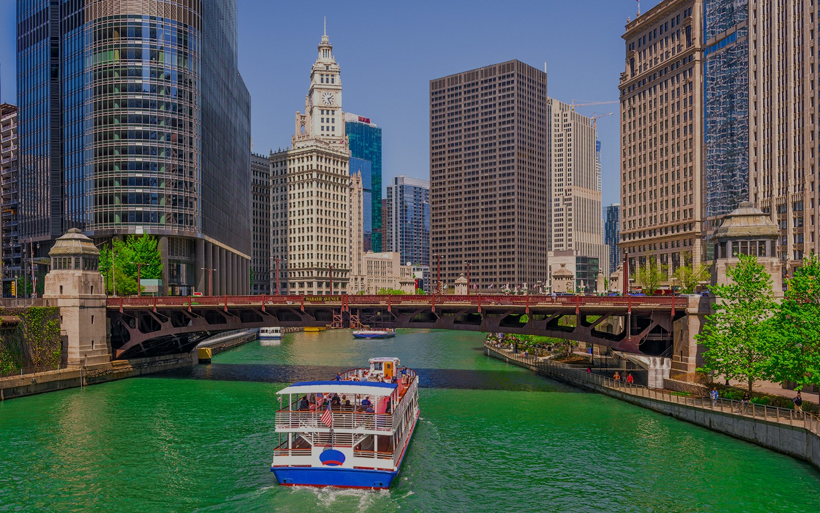 Cruise boat on Chicago River with city skyscrapers and Wrigley Building in view.