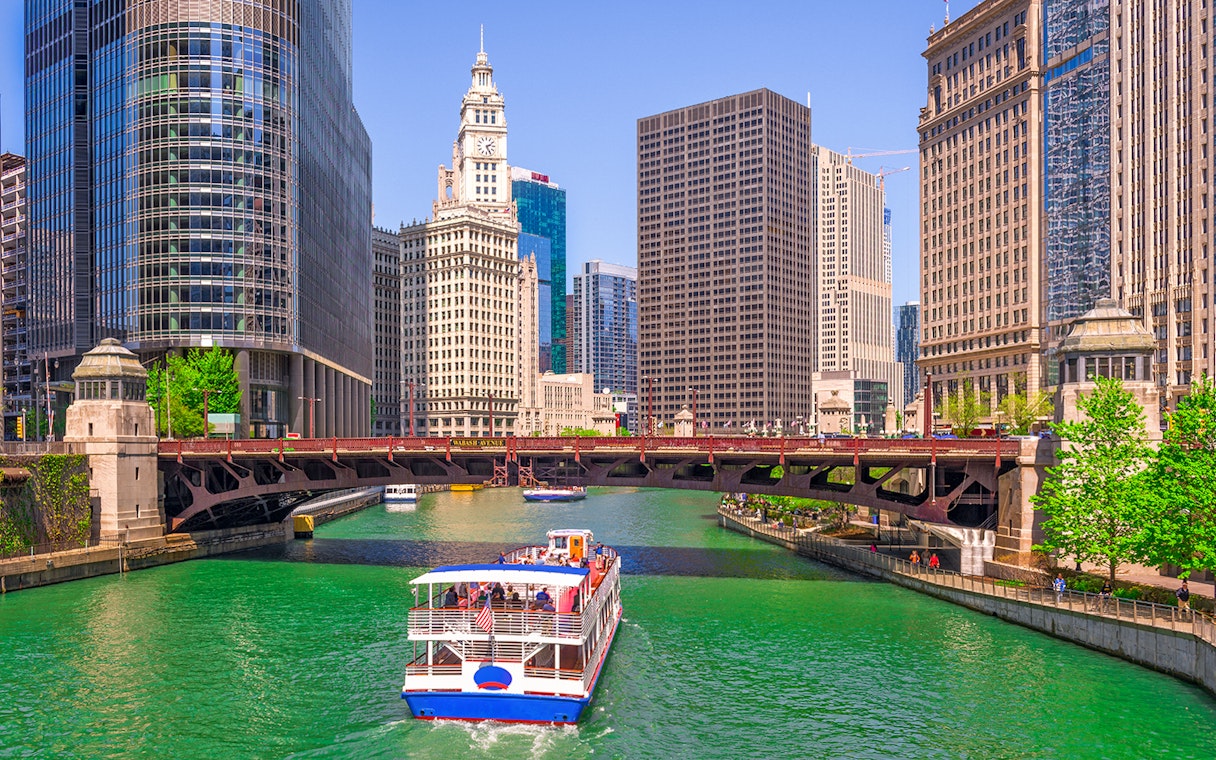 Cruise boat on Chicago River with city skyscrapers and Wrigley Building in view.