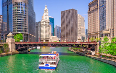 Cruise boat on Chicago River with city skyscrapers and Wrigley Building in view.