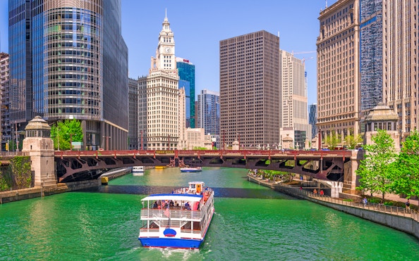Cruise boat on Chicago River with city skyscrapers and Wrigley Building in view.