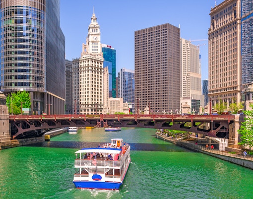 Cruise boat on Chicago River with city skyscrapers and Wrigley Building in view.