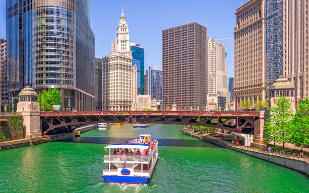 Cruise boat on Chicago River with city skyscrapers and Wrigley Building in view.
