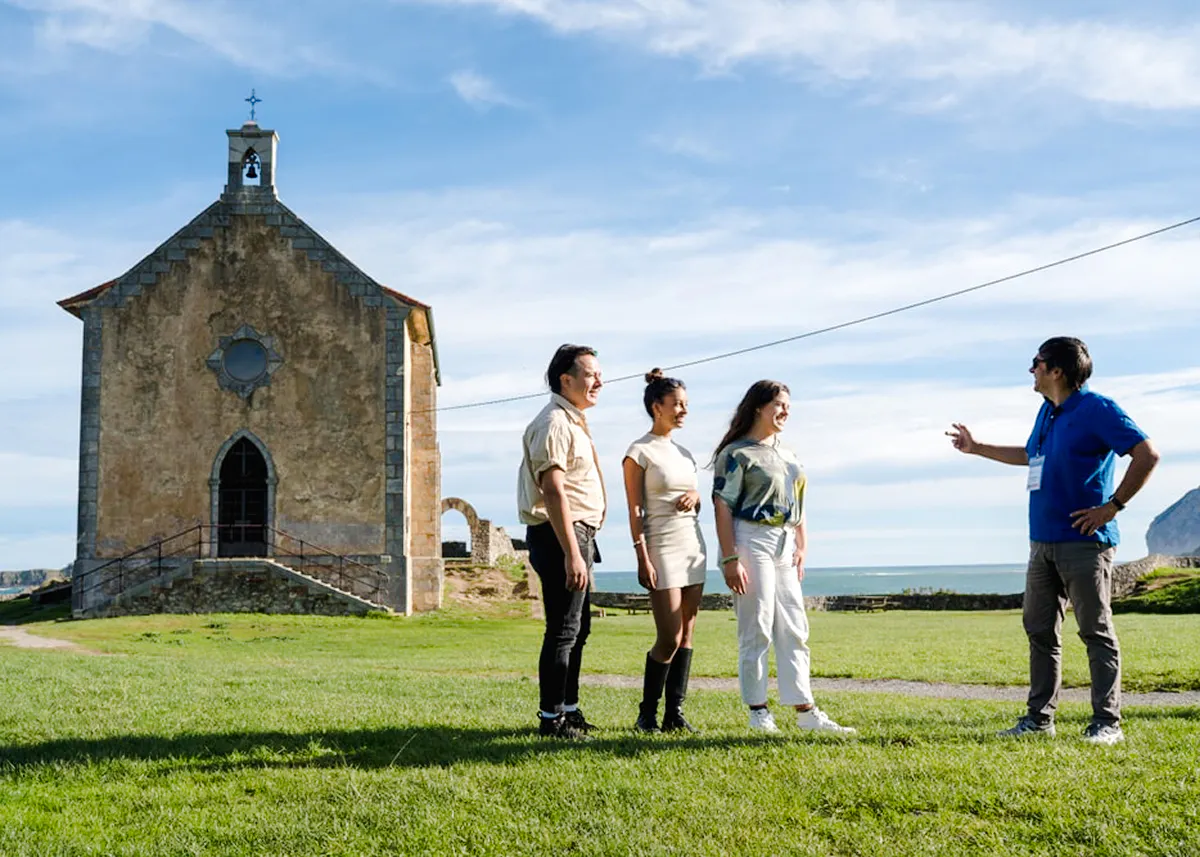 Tour group at chapel near Dragonstone, Mundaka, with ocean view in background.