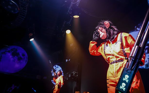 Performers in monkey masks and orange suits on stage at WARP Shinjuku Nightclub.